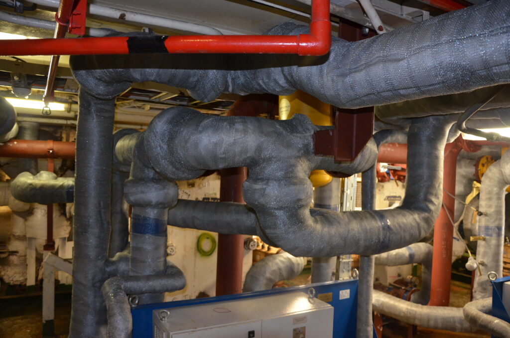 Wärmeisolierte Rohrleitungen mit grauer Gewebeabdeckung in Pumpenraum